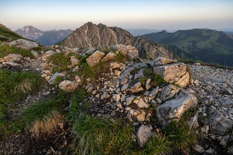Felsen und Gras mit Blick auf bergige Landschaft im Hintergrund bei Sonnenaufgang.